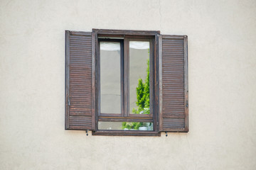 Italian window on the sandy yellow wall facade with open brown color wooden classic shutters