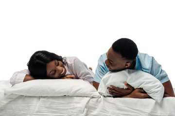 happy african american couple lying in bed in pajamas isolated on white