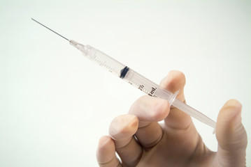 A hand with a surgical glove holds an medical injection.
