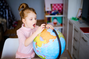 Young caucasian girl looking at earth globe at home. Schoolgirl doing homework and showing something at the globe