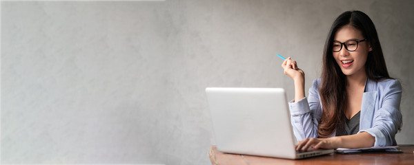 Young happy Asian businesswoman in blue shirt working from home and use a computer laptop and...