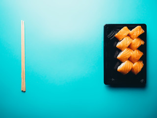 Food delivery, Philadelphia rolls in a black box with chopsticks. Blue background.