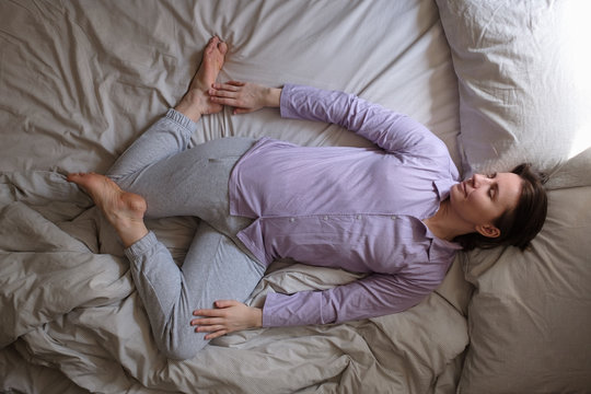 Young caucasian woman working out at home at the bed doing Spinal Twist