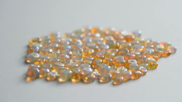 Opals gemstone from Ethiopia rotates on light background. White fire opals with rainbow like fire. Natural fire Ethiopian opal, small stones to create jewelry. Handmade stone jewelry. A pile stones.