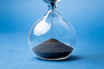 Sand runs in the hourglass, measuring the travel time in the countdown to the deadline on blue background