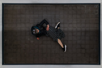 Young women with blue hair, sunglasses and leather jacket laying on tiled floor