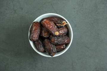Raw date fruit ready to eat in porcelain bowl on concrete background. Traditional, delicious and healthy ramadan food. Top view, flat lay.