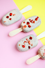 Eskimo ice cream on stick in chocolate glaze and red sublimated strawberry on yellow and pink background. Yummy sweet food snack treat. Top view, close-up, diagonal