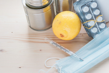 .thermometer, canned food, lemon and two piles of tablets on a wooden background