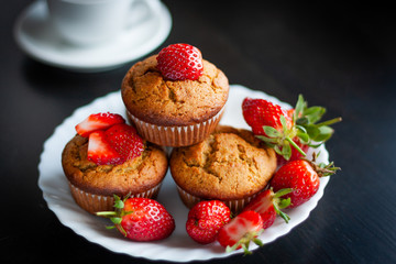 Homemade muffins with fresh strawberries on white plate on black table. Homemade tasty dessert or breakfast. Healthy eating concept