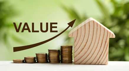 Model of house and stacked coins on table against blurred green background. Growing value