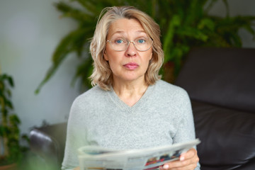 news, press, media, holidays and people concept - woman reading newspaper at home