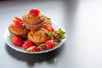 Homemade muffins with fresh strawberries on white plate on black table. Homemade tasty dessert or breakfast. Healthy eating concept