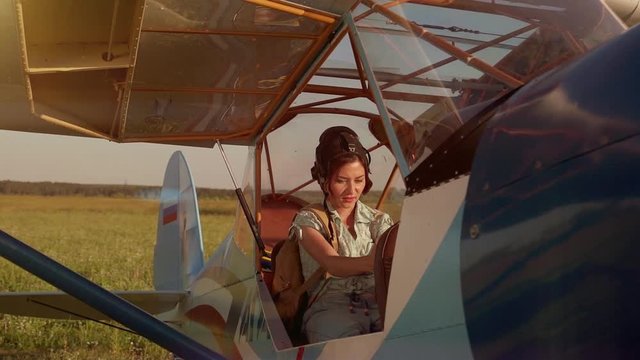 Young adventurous woman pilot in old airplane at summer sunset. Freedom, extreme and feminism concept. Breathtaking adventure in the air. Proffesional captain girl preparing for flight and skydiving