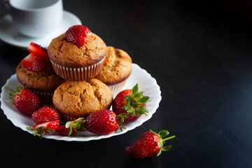Homemade muffins with fresh strawberries on white plate on black table. Homemade tasty dessert or breakfast. Healthy eating concept
