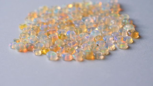 Opals gemstone from Ethiopia rotates on light background. White fire opals with rainbow like fire. Natural fire Ethiopian opal, small stones to create jewelry. Handmade stone jewelry. A pile stones.