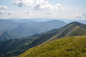 View from the top of Carpathian Mountains, grassy meadow of a hillside under the blue sky with clouds in summer day, Ukraine