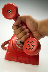 A hand picking up the handset of a red vintage old rotary phone.