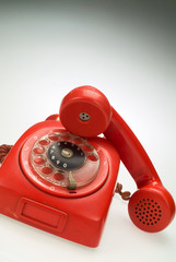A a red vintage old rotary phone with handset picked up.