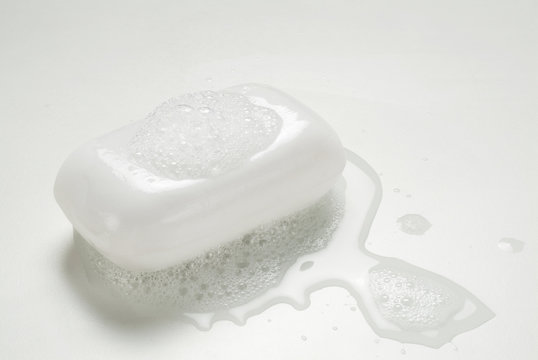 A wet bar of regular white soap bar with bubbles and water.
