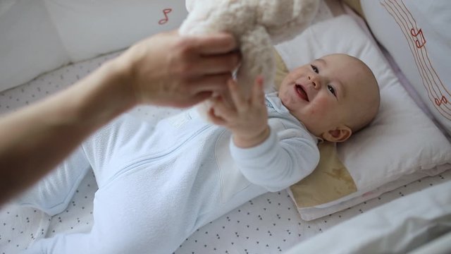 Little baby stretches hands to mom trying to catch a teddy bear