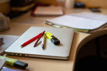 3 pens and pencils over a laptop on a Table for studying full of papers and books