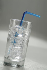 An cold ice water glass with blue straw.