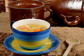 A mug full of broth with noodles next to clay pots