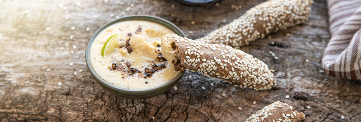 freshly baked fresh homemade breadsticks with sesame, homemade mayonnaise, hummus or white sauce on a wooden table. Country food. Rustic style.