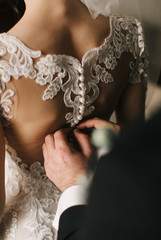 Back view of a bride in a wedding dress and groom helping her to dress