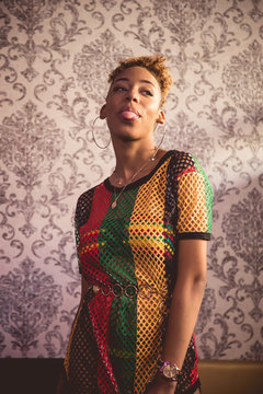 Portrait of a black girl with her hair tied up, big earrings and a colorful net dress showing her tongue with a funny expression