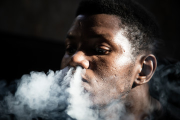 Portrait of a black young man smoking from his nose sitting in a dark room