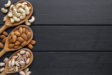 nuts in wooden bowl. Assortment of nuts - cashew, hazelnuts, walnuts, pistachio, pecans, pine nuts, peanut, raisins  on black background.Healthy snack, vegetarian food, Top view.