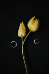 Two yellow tulips with wedding rings on black background