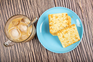 Cup of cold coffee with Crackers on a plate on wooden background.