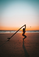 Portrait fitness girl posing with surfboard on the beach at sunset with silhouette