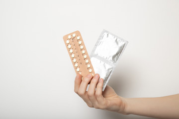 Girl holds birth control pills and condoms on white background