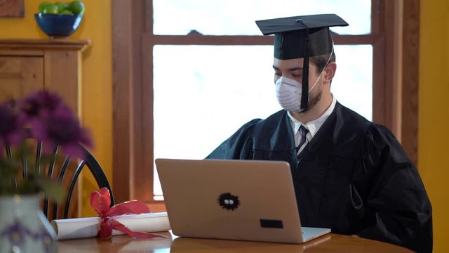 Young man graduation online in quarantine wearing face mask and holding diploma out for portrait.