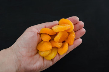 ripe dried apricots in a palm on a black background. View from above. Close-up. A handful of delicious dried apricots.