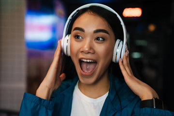 Photo of asian woman using wireless headphones and singing in cafe
