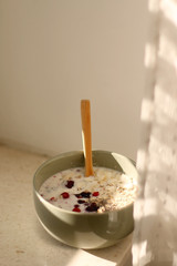Breakfast bowl with oatmeal, berries and coconut chips, illuminated by morning sunlight. Selective focus.