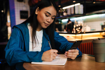 Photo of asian woman making notes and using cellphone