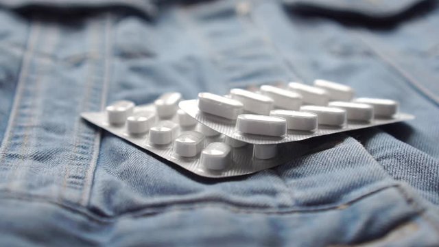 Coronavirus drug. Two packs of white pills fall onto denim. Close-up. Slow motion. The use of paracetamol in the fight against coronavirus