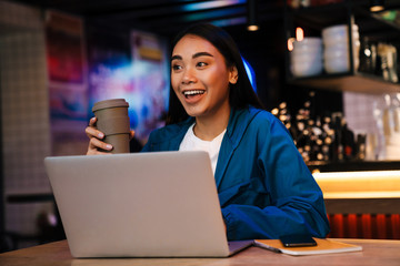 Photo of asian woman working with laptop and drinking coffee in cafe