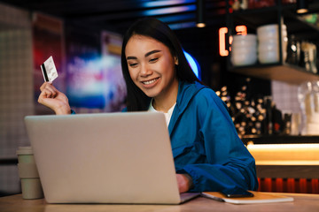 Photo of young asian woman working with laptop and holding credit card