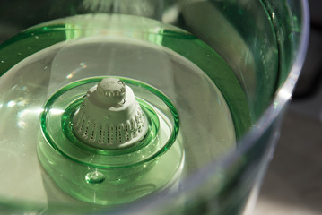 Close-up of a jug with a water purification cartridge. Green. The cartridge shows air bubbles under the water. The concept of purification. - obrazy, fototapety, plakaty