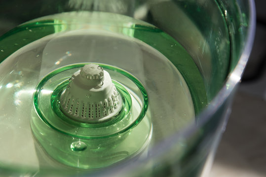 Close-up of a jug with a water purification cartridge. Green. The cartridge shows air bubbles under the water. The concept of purification.