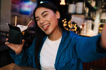 Photo of asian woman holding noodles and winking while taking selfie