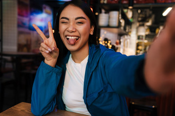 Photo of asian woman gesturing peace sign while taking selfie