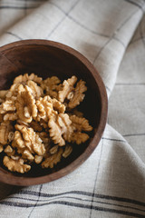 Wooden bowl full of walnuts on a gray napkin.